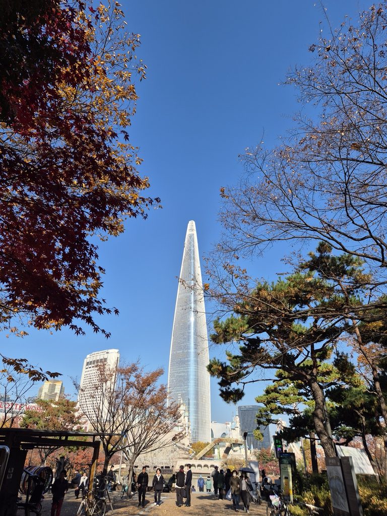 Lotte World Tower rising above autumn trees in Jamsil, Seoul