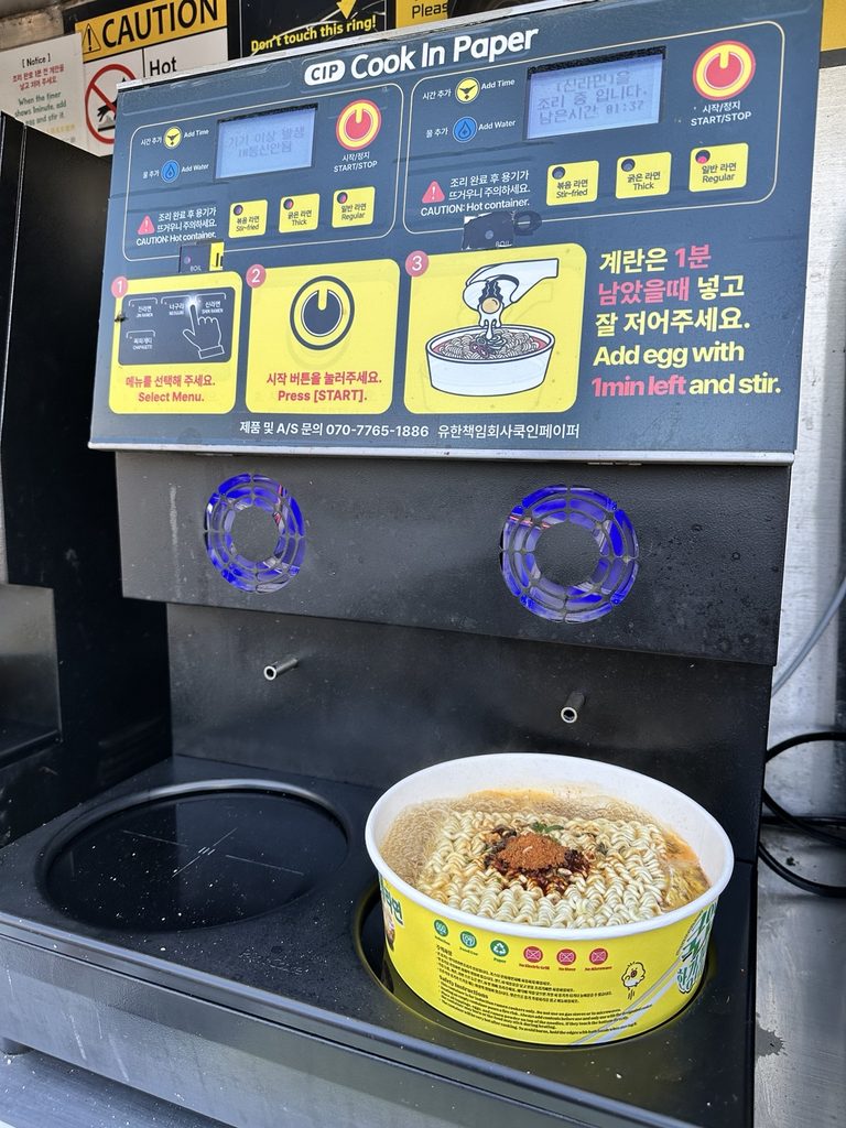 Korean instant ramen cooking in a paper bowl on an automatic ramen machine at a CU convenience store in Banpo Hangang Park, Seoul.